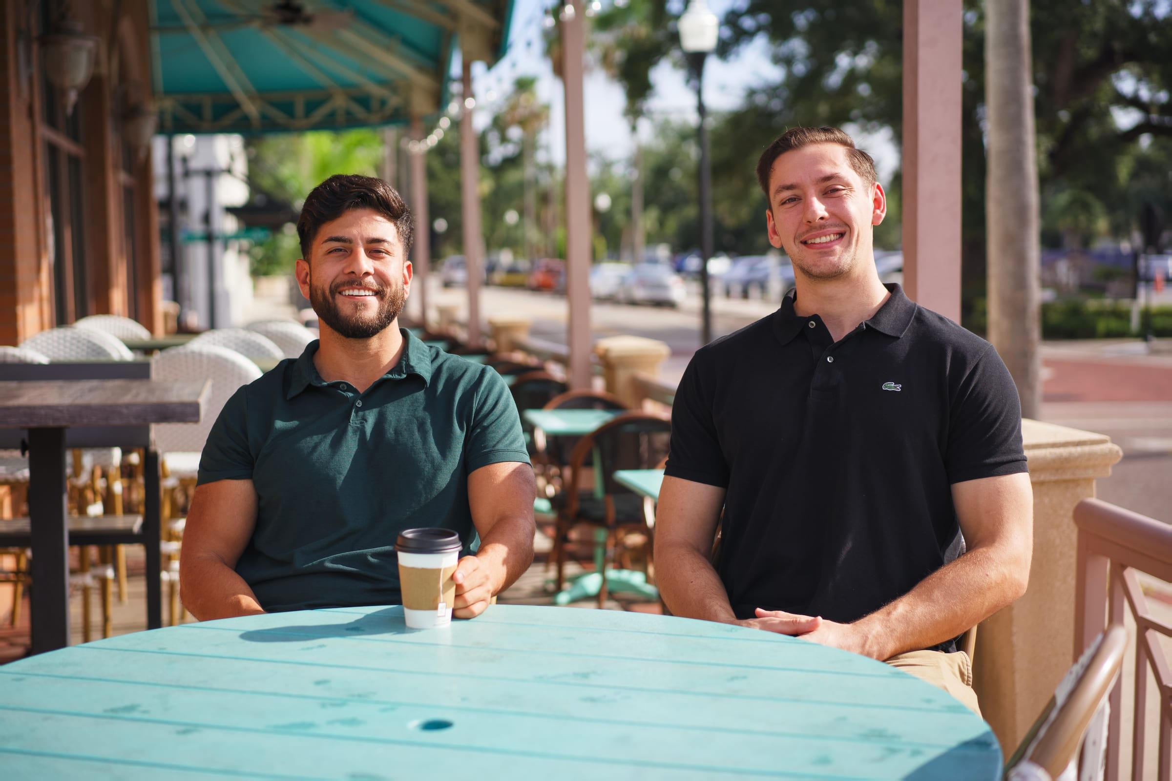 Nate Levi and Uğur Karabiyik, co-founders of Bay Web Digital, sitting at an outdoor café table in the Tampa Bay area